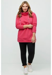 Fuchsiový svetr s vysokým límcem a šňůrkami, kombinovaný s černými slim-fit kalhotami a bílými teniskami. Měkká tkanina a volný střih.