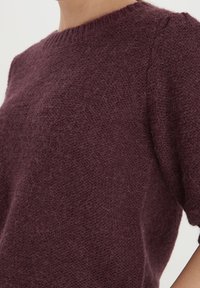 Burgundy stickad tröja med korta puffärmar. Tillverkad av mjukt, strukturerat tyg med rundad halsringning och en avslappnad passform.