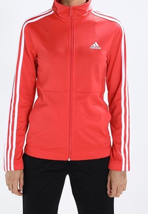 Red Adidas zip-up jacket with white stripes on sleeves and logo on chest, worn with black pants.