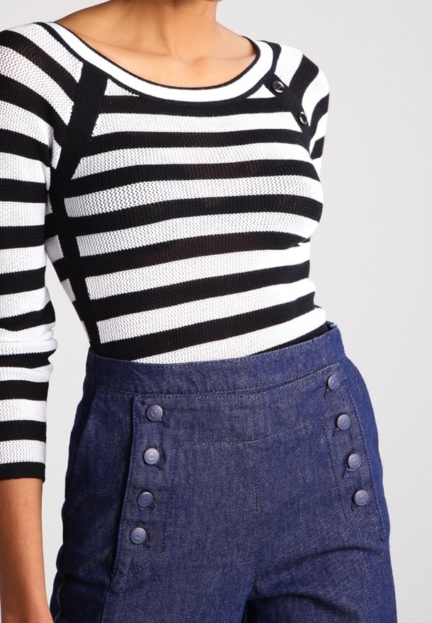 Top de punto a rayas en blanco y negro con un escote ancho, combinado con pantalones vaqueros de cintura alta en denim azul que presentan botones decorativos en la parte delantera.