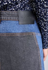 Jupe en denim avec un design patchwork comprenant des sections bleues claires et foncées, étiquette en cuir avec "MUNTHE" embossé et couture renforcée.