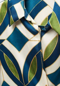 Seidenhemdkragen mit geometrischem Muster in Blau-, Grün- und Cremetönen, das mit goldenen Rauten- und Ovalformen umrissen ist.