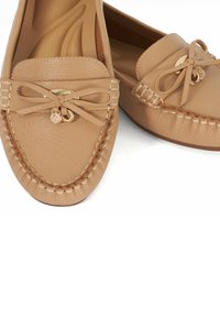 Mocassins en cuir beige avec un design cousu, accent de nœud et détail en métal doré. Surface texturée et forme de pointe arrondie.