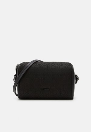 Sac bandoulière noir Calvin Klein avec motif de logo en relief et sangle réglable sur un fond uni clair.