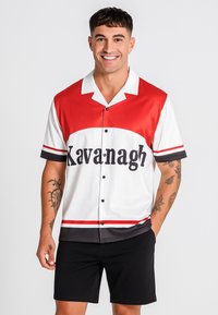 Camisa de botones de manga corta en rojo y blanco con un estampado llamativo de "Kavanagh", acentos y rayas negras, combinada con pantalones cortos negros.