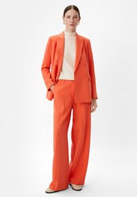 Pomarańczowy podwójnie zapinany żakiet z szerokimi spodniami, w połączeniu z kremowym golfem. Gładki materiał, dopasowany krój oraz minimalistyczny design.