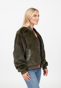 Olivgrüne Kunstfell-Bomberjacke, gerippte Bündchen und Saum, Reißverschluss vorne, Seitentaschen mit Akzentnähten und Logopatch.