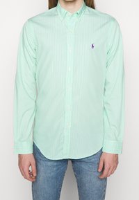 Light green long-sleeve shirt with white vertical stripes, button-down collar, front buttons, and a small purple logo on the chest.