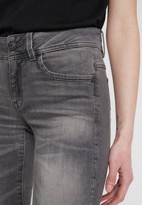 Grå denimjeans med mid-rise midja, subtil slitage, femficksdesign och knäppning. Mjuk textur och lätt blekning.