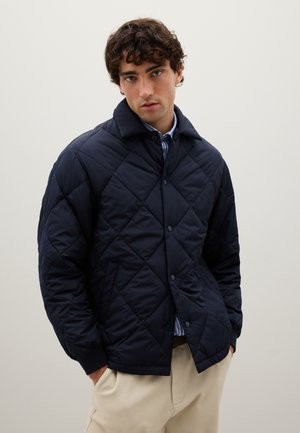 Navy quilted jacket features a diamond pattern, a button-up front, and a collared neckline. Soft, padded material and side pockets.