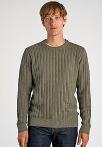 Pull en laine verte tricoté avec un design en câble texturé, col rond et poignets et ourlet côtelés, assorti à un jean en denim foncé.