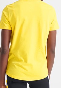 Camiseta de algodón amarilla de manga corta con cuello redondo; textura suave, diseño ajustado y sin logos ni acentos visibles.