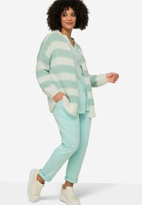 Cardigan a righe verde menta con vestibilità ampia, abbinato a pantaloni verdi menta e sneakers bianchi. Texture morbida in maglia, design casual.