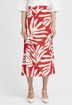 Rode midi-rok met groot gebroken wit bladmotief, gedragen met een witte top en witte pumps met spitse neus en enkelriempjes.