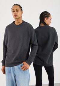 Mørkegrå crewneck sweatshirt i blødt stof, med lange ærmer og afslappet pasform. Bæres med lyseblå jeans og sorte tætsiddende leggings.