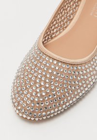 Ballerine con tomaia in tessuto beige, decorate con numerosi strass trasparenti, foderatura interna morbida e design del tallone in rete aperta.