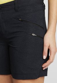 Mörk marinblå shorts med en texturerad tyg, med två vinklade dragkedjefickor och en slät fåll. Handen placerad på midjebandet.