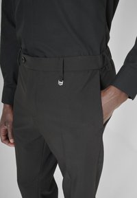 Pantalones negros con una textura suave, que cuentan con un cinturón con hebilla plateada, bolsillos frontales y una pretina ajustada.