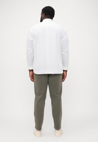 Chemise blanche à boutons, à manches longues, associée à un pantalon vert olive et à des baskets de couleur claire. Tissu doux, coupe décontractée et design simple.