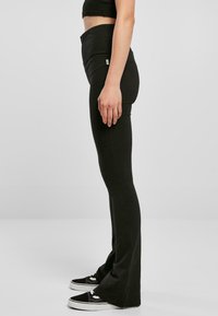 Leggings noires évasées avec une taille haute, en tissu élastique. Portés avec des chaussures noires à semelles et lacets blancs.