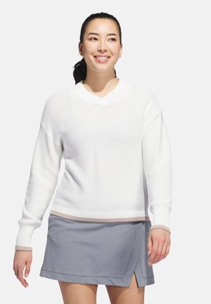 Hvid strikket sweater med V-udskæring og ribbede manchetter, parret med en lysegrå nederdel med en omslagdesignet og fremhævende søm.