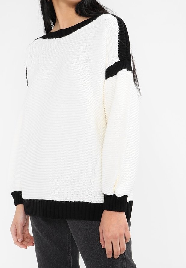 Pull à blocs de couleurs en blanc avec des accents noirs, présentant un tricot texturé, une coupe oversize et des poignets et ourlet côtelés.