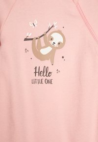 Rózsaszín pulóver, amelyen egy lajhár lóg egy ágról, alatta a "Helló Kicsi" felirattal, lágy színekkel illusztrálva.