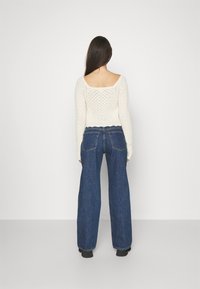 Pletený krémový top s dlouhým rukávem a čtvercovým výstřihem, kombinovaný s modrými džínami s vysokým pasem a širokými nohavicemi.