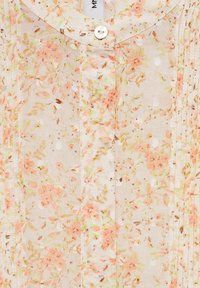 Blouse légère à fleurs avec une base crème ornée de motifs floraux roses et verts, un col arrondi et une fermeture à boutons.