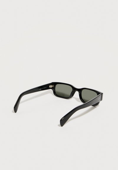 Μαύρα ορθογώνια γυαλιά ηλίου με σκουρόχρωμους φακούς τοποθετημένα ανοιχτά πάνω σε λευκή επιφάνεια, εμφανιζόμενα από οπίσθια κεκλιμένη γωνία.