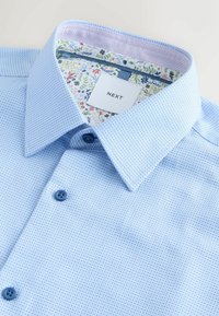 Lyseblå textured skjorte med et mønstret indre krave. Har to blå knapper og en etiket med mærkenavnet "NEXT".