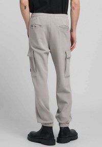 Pantaloni jogger grigio chiaro con polsini a costine, due tasche posteriori e tasche cargo laterali. Realizzati in tessuto morbido con vestibilità rilassata.