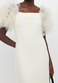 Spitzenkleid in Off-White mit quadratischem Ausschnitt und Tüll-Puffärmeln. Verfügt über ein florales Muster und eine taillierte Passform.