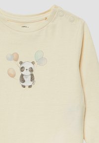 Hellcremefarbenes Langarmshirt mit einem Panda-Motiv, der drei bunte Luftballons hält, und Druckknöpfen auf der linken Schulter. Weiche Textur.