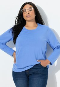 Blauw T-shirt met lange mouwen van zacht stof met een ronde hals, gecombineerd met een donkere spijkerbroek, met een relaxte pasvorm en minimale naden.