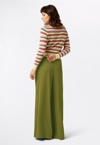 Gestreifter Strickpullover in verschiedenen Farben mit schmalen Bündchen, kombiniert mit hochgeschnittenen, weit geschnittenen grünen Hosen. Glatte Textur und lässiges Design.