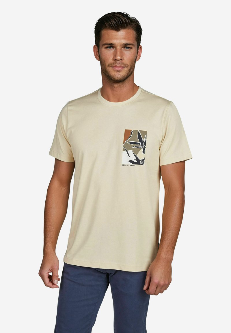 Beige Baumwoll-T-Shirt mit Rundhalsausschnitt und kurzen Ärmeln, ausgestattet mit einem quadratischen Taschen-Design mit einem schwarzen und braunen Blattmuster.