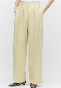 Pantalons larges plissés en tissu jaune clair, dotés de poches latérales et d'une taille haute, associés à des chaussures texturées à imprimé serpent.