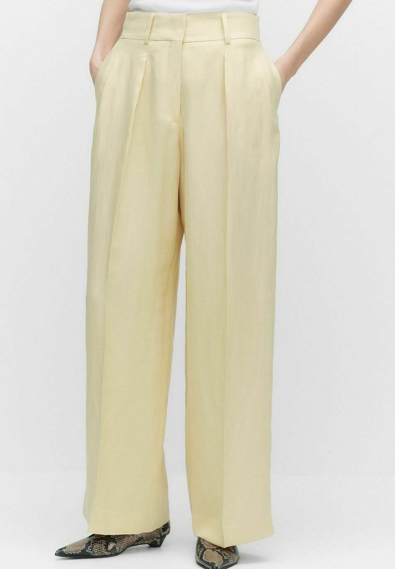 Pantalons larges plissés en tissu jaune clair, dotés de poches latérales et d'une taille haute, associés à des chaussures texturées à imprimé serpent.