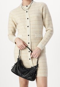 Robe tricotée à manches boutonnées en plaid crème et beige avec des boutons noirs et des poches, associée à un sac à main en cuir noir avec des accents en chaîne.