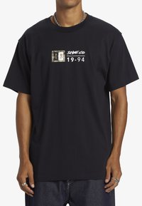 Black cotton t-shirt featuring a white graphic logo with a camouflage square and "Side Co 19-94" text on the chest. Short sleeves, relaxed fit.