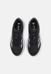 Schwarze Sportschuhe mit texturiertem Obermaterial, ausgestattet mit drei grauen Streifen, einer gepolsterten Zunge und einer gedämpften weißen Sohle.