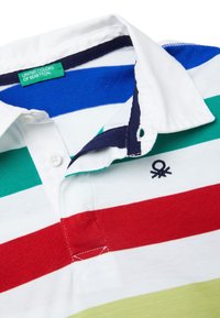 Polokošile v bílé barvě s horizontálními pruhy v červené, zelené, modré a světle zelené barvě. Má tmavě modrý límec a na hrudi vyšívané logo.