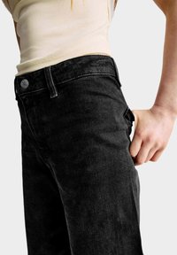 Zwarte denim spijkerbroek met een rechte pasvorm en subtiele textuur. Inclusief voorzak en knoopsluiting. Gemaakt met een lichtgekleurde top.