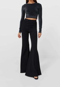 Pantaloni neri a palazzo con una texture liscia, abbinati a un crop top lungo a manica con luccichii scuri. Entrambi gli articoli presentano una silhouette aderente.