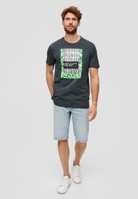 Donkergrijze katoenen T-shirt met een groen en zwart bedrukt ontwerp met het woord "flowers." Gepaard met lichtblauwe denimshorts en witte sneakers.