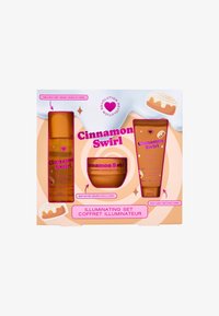 Conjunto iluminador de canela enrollada que incluye bruma corporal de naranja, manteca corporal y gel de ducha, presentado en una caja en tonos pastel rosa y naranja con gráficos de postres.