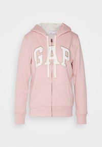 Felpa rosa con zip, foderata in pile bianco, con cordini bianchi, tasche frontali e grandi lettere bianche "GAP" ricamate sul petto.