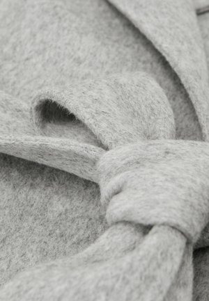 Tela de fieltro gris con textura suave, que presenta un detalle de lazo anudado. El diseño incluye pliegues superpuestos que realzan la profundidad.