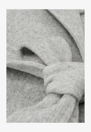 Tela de fieltro gris con textura suave, que presenta un detalle de lazo anudado. El diseño incluye pliegues superpuestos que realzan la profundidad.